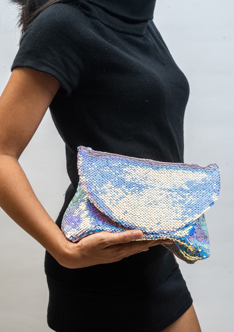 Person holding a silver sequin clutch against a plain background