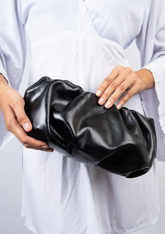 Person holding a black leather clutch against a white background