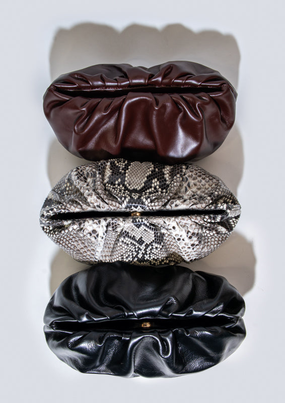 Three leather clutch handbags in Bordeaux, black, and snake print on a white background