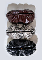Three leather clutch handbags in Bordeaux, black, and snake print on a white background